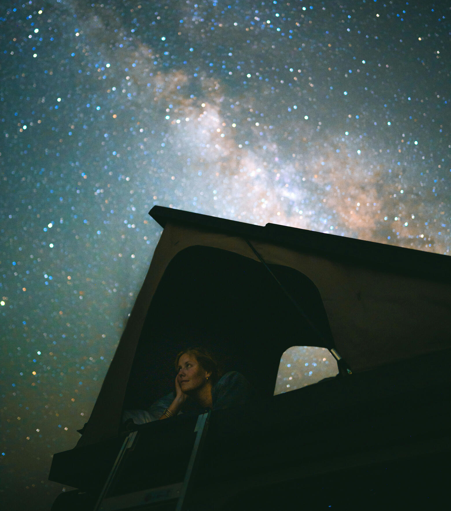 Woman stargazing from a glamping tent under the Milky Way — magical eco-travel and stress-free outdoor adventure.
